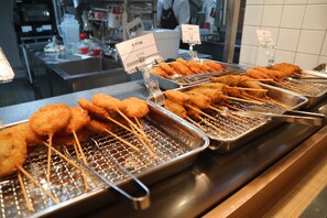 A buffet with various fried items on skewers, trays, and a grill.