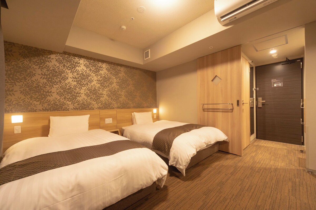 A hotel room with two beds, a wooden headboard, a patterned wall, and a door with a handle.