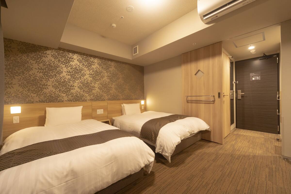 A hotel room with two beds, a wooden headboard, a patterned wall, and a dark door.