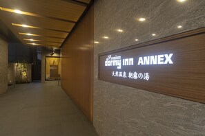 A hotel entrance with a sign reading "Premium Dormy Inn Annex" and a wooden panel design.