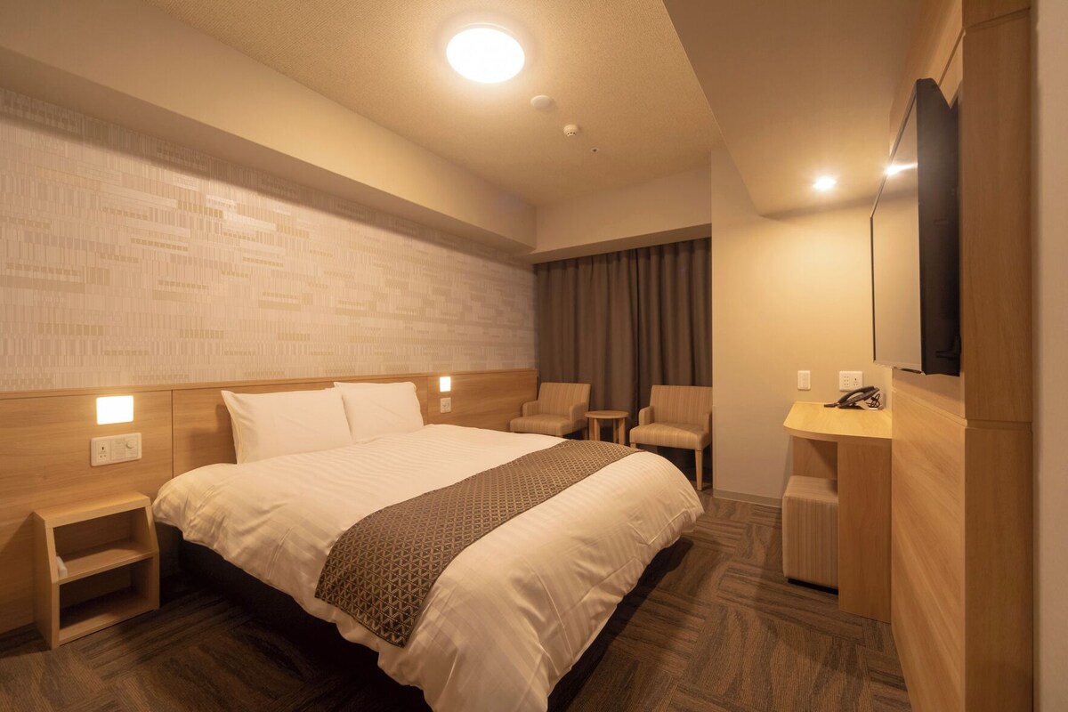A hotel room with a large bed, bedside tables, a desk with a telephone, and a mirror on the wall.