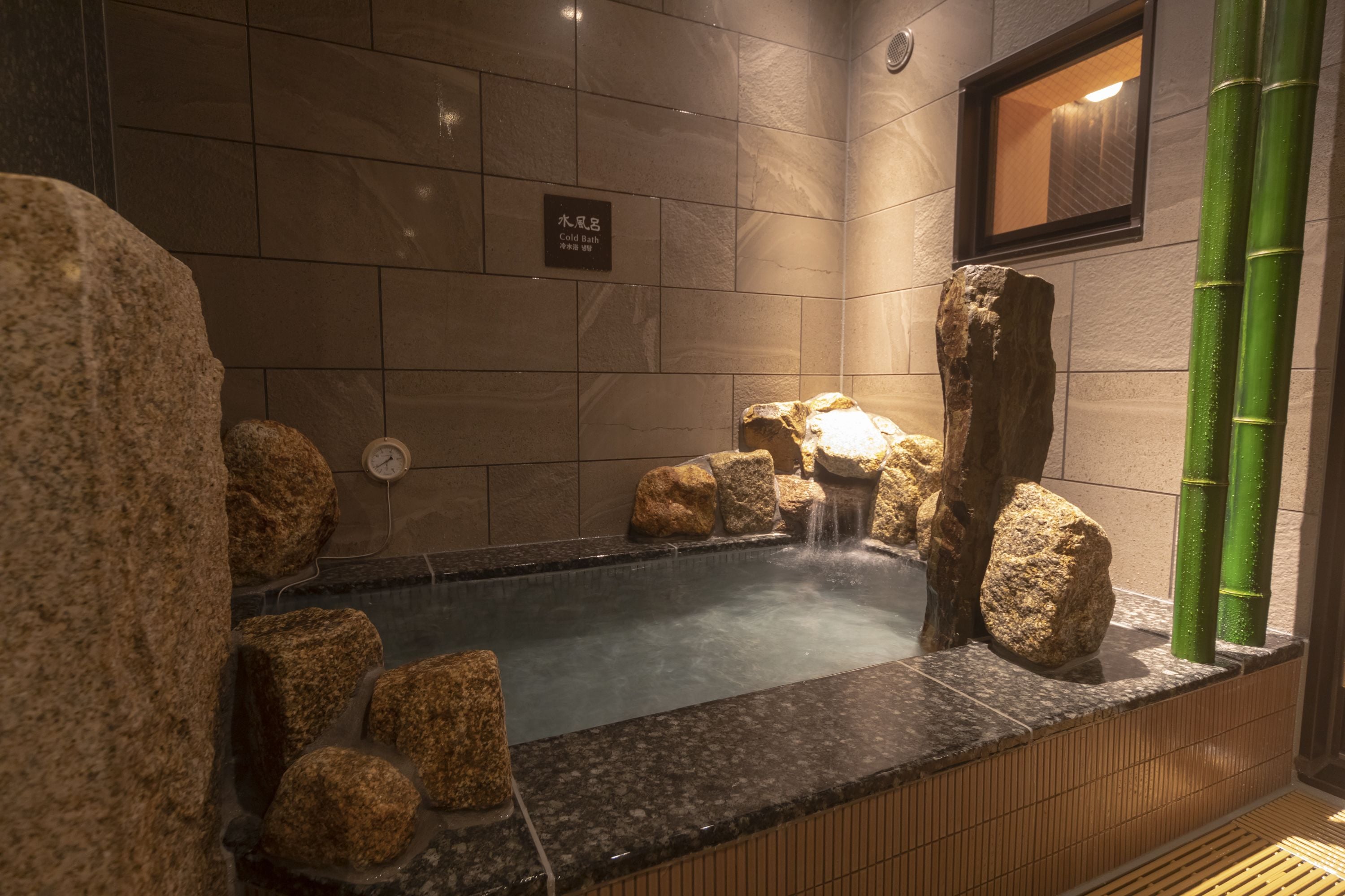 A hot spring bath area with a tiled wall, a wooden platform, and several large rocks.