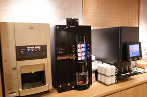 A coffee machine and a tea dispenser on a counter with a digital screen and cups.
