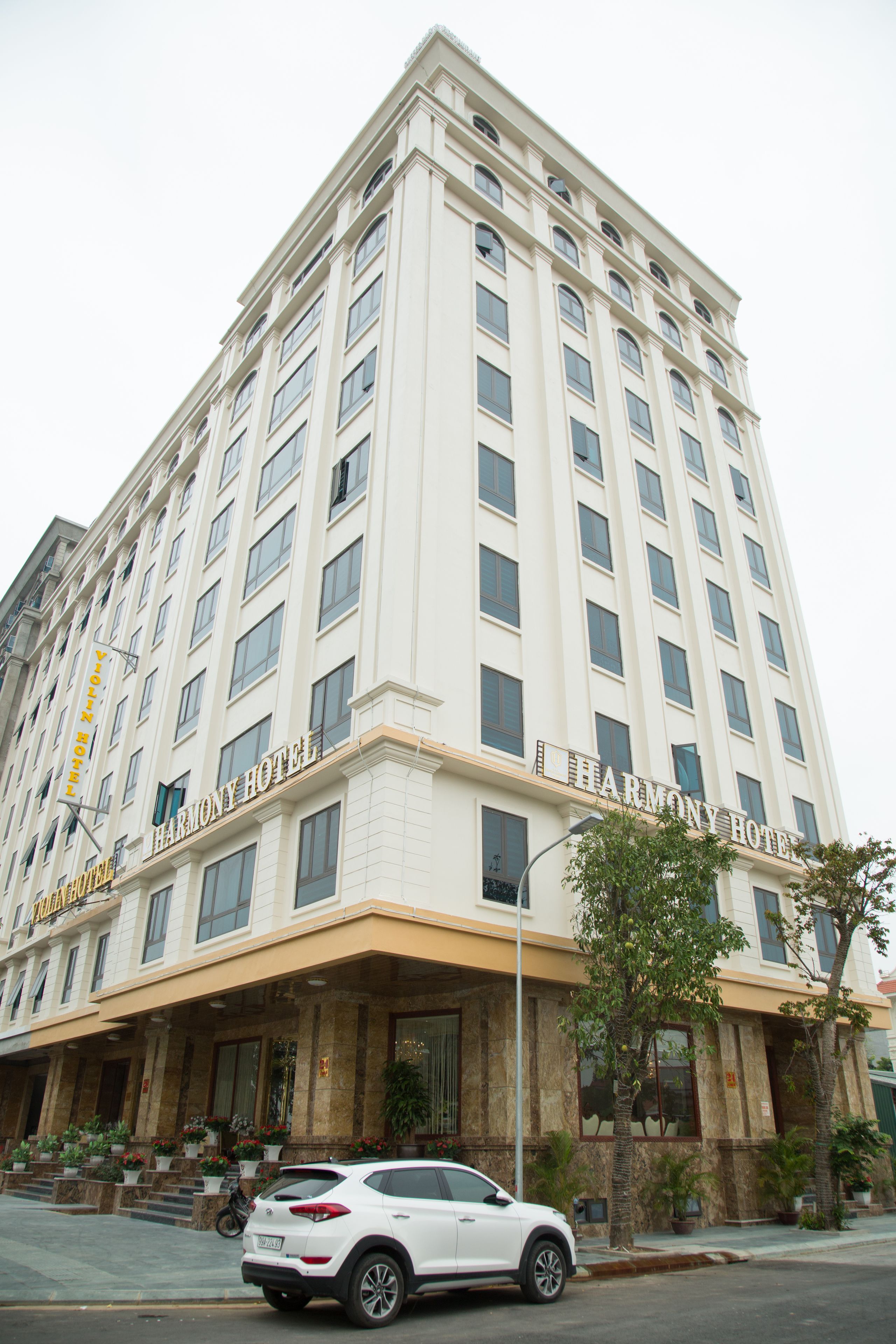 A multi-story Harmony Hotel building with a prominent entrance and a white car parked in front.
