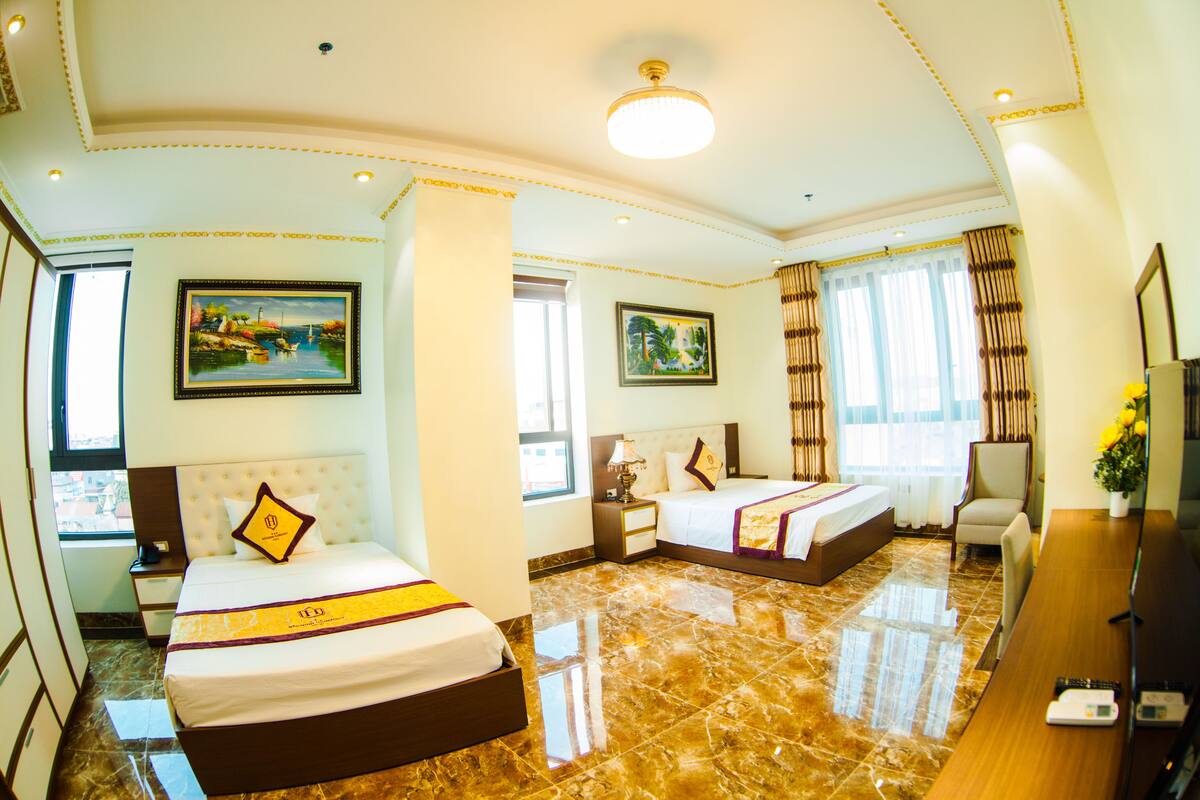 A hotel room with two beds, a desk, a chair, and two paintings.