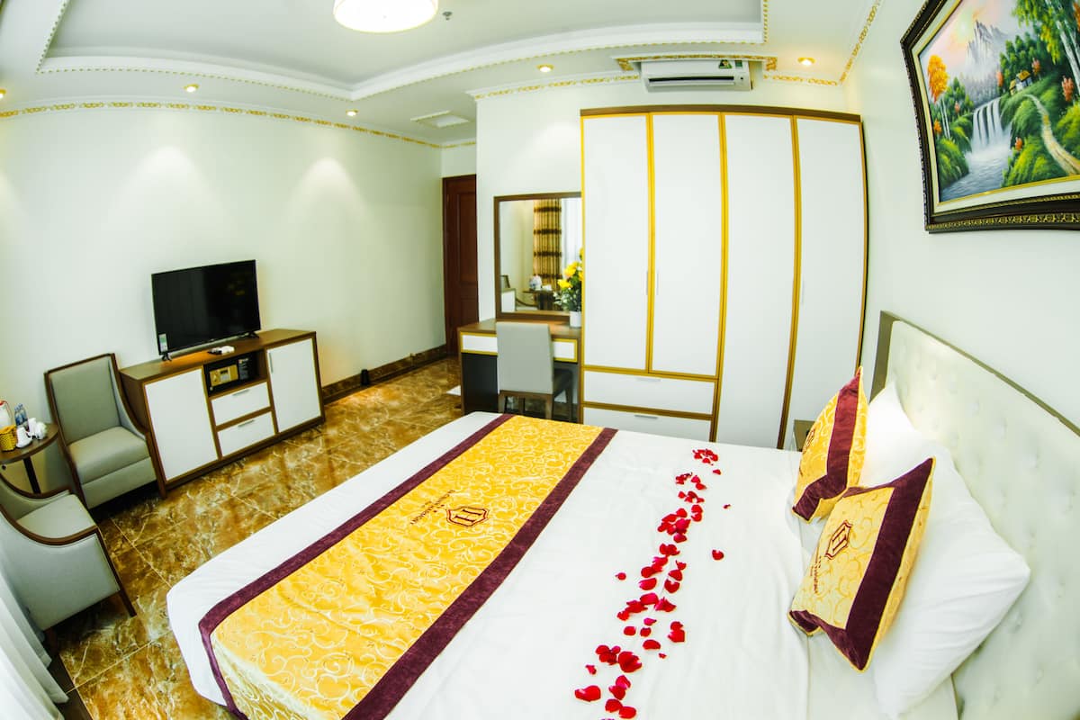 A hotel room with a large bed, a television, a desk, and a mirror.