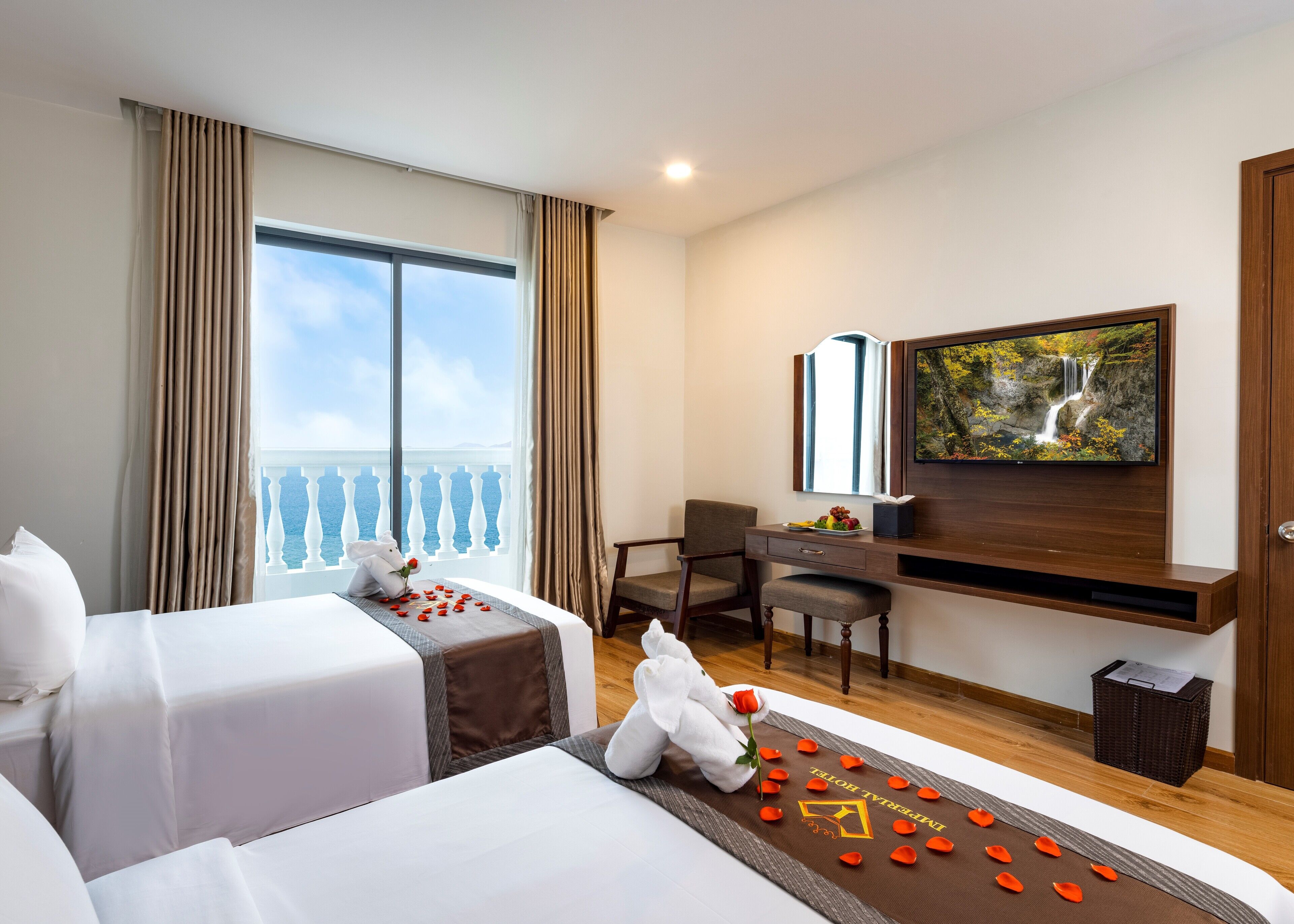 Een hotelkamer met twee bedden, een bureau, een televisie en een balkon met uitzicht op zee.