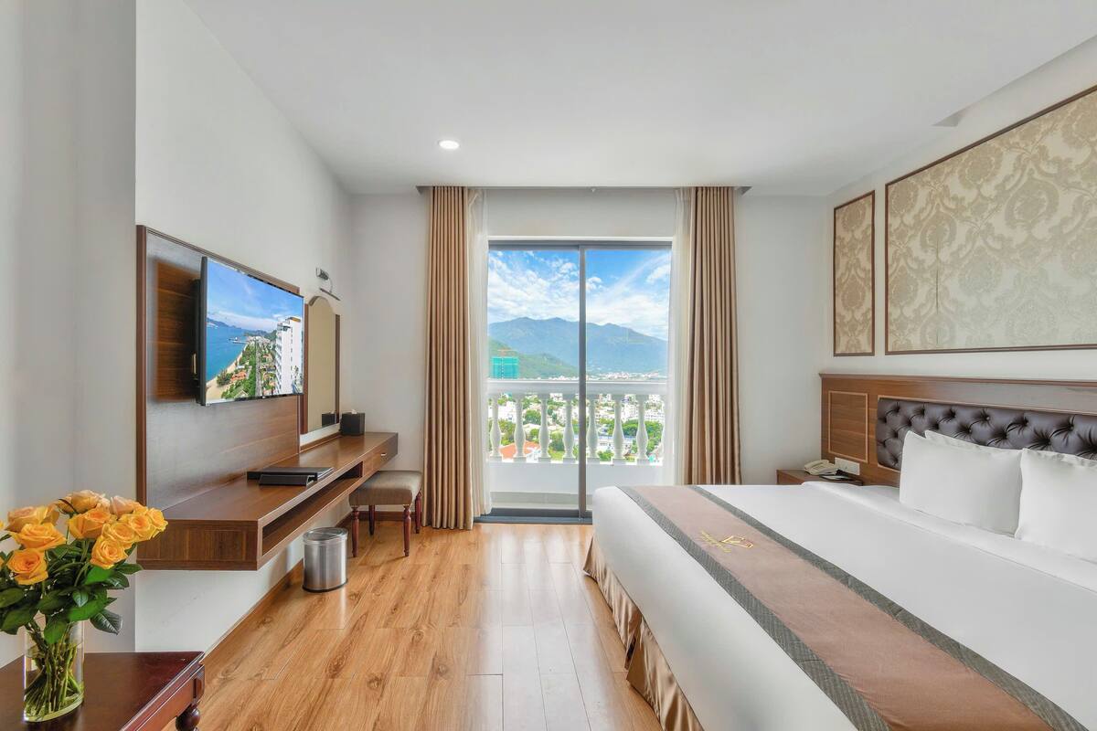 A hotel room with a bed, a desk, a TV, and a balcony with a view.