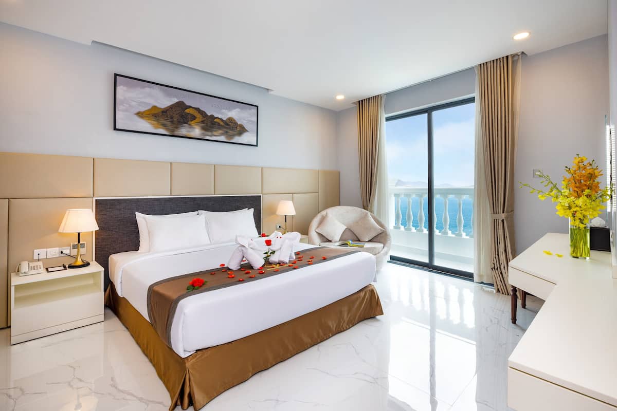 A modern hotel room with a large bed, a desk, and a balcony with a view.