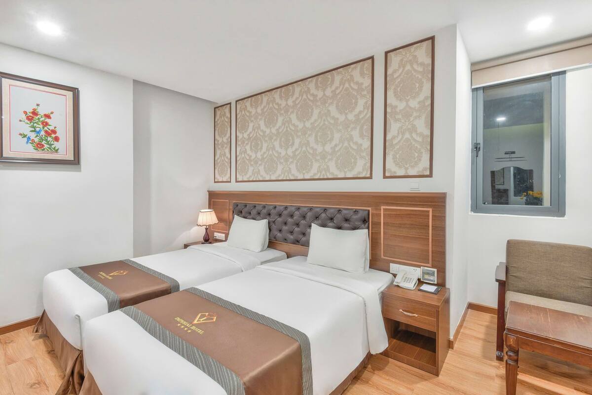 A hotel room with two beds, a nightstand with a phone, a lamp, and a window with a city view.