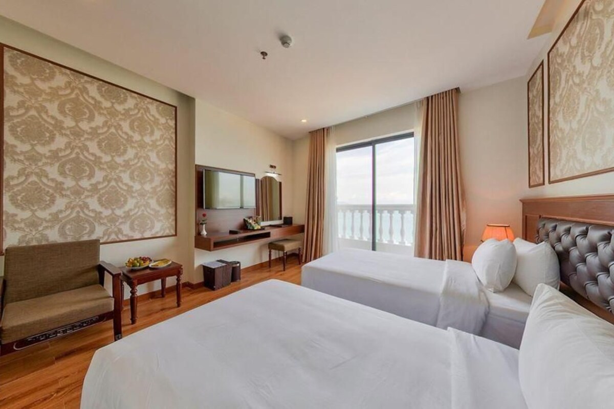 A hotel room with two beds, a desk with a chair, a television, and a balcony with curtains.