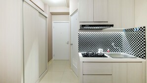 A narrow kitchen with a checkered backsplash, a gas stove, and a sink. - Studio at Green Pramuka City Serene Apartment Living By Travelio (Jakarta)