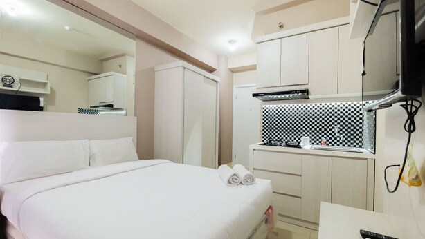 A hotel room with a bed, a small kitchenette, a TV, and a mirror. - Studio at Green Pramuka City Serene Apartment Living By Travelio (Jakarta)