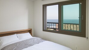 Une chambre à coucher avec un lit, une fenêtre donnant sur la mer et un balcon avec une balustrade.