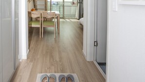 Un couloir avec un plancher en bois, un coin repas avec une table et des chaises, un escalier et une porte donnant sur une pièce où se trouve un lit.