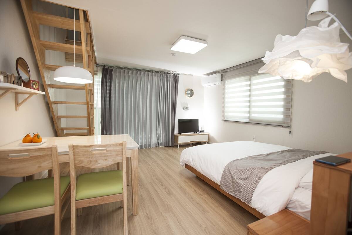 A bedroom with a bed, bedside table, lamp, TV, and a desk with chair.