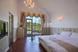 A bedroom with a large bed, a chandelier, a balcony with a view, and a television. - Beauty Spring and Harvest B and B (Puli)