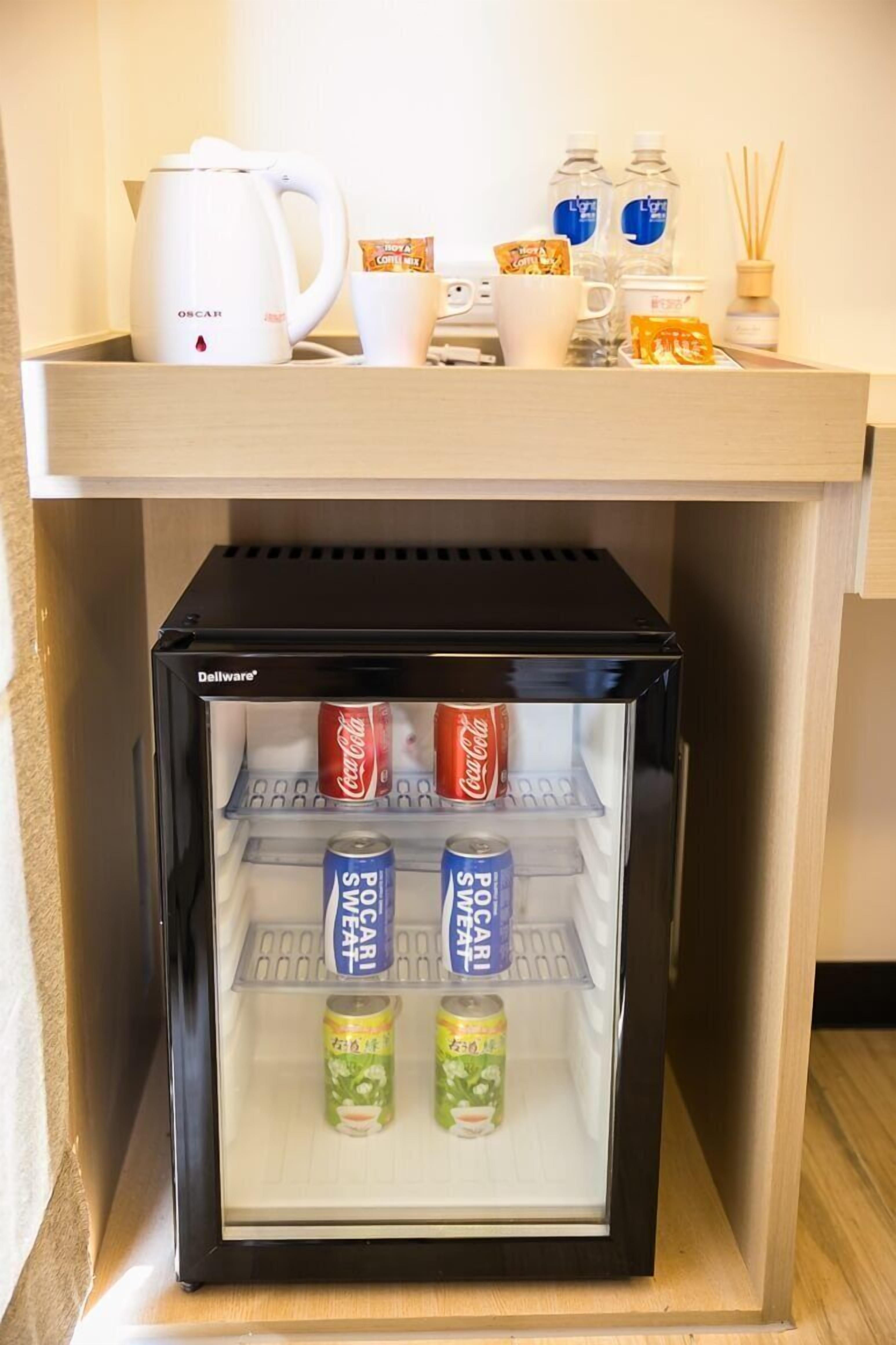 A compact refrigerator with a transparent door, containing beverages and a coffee maker on top.