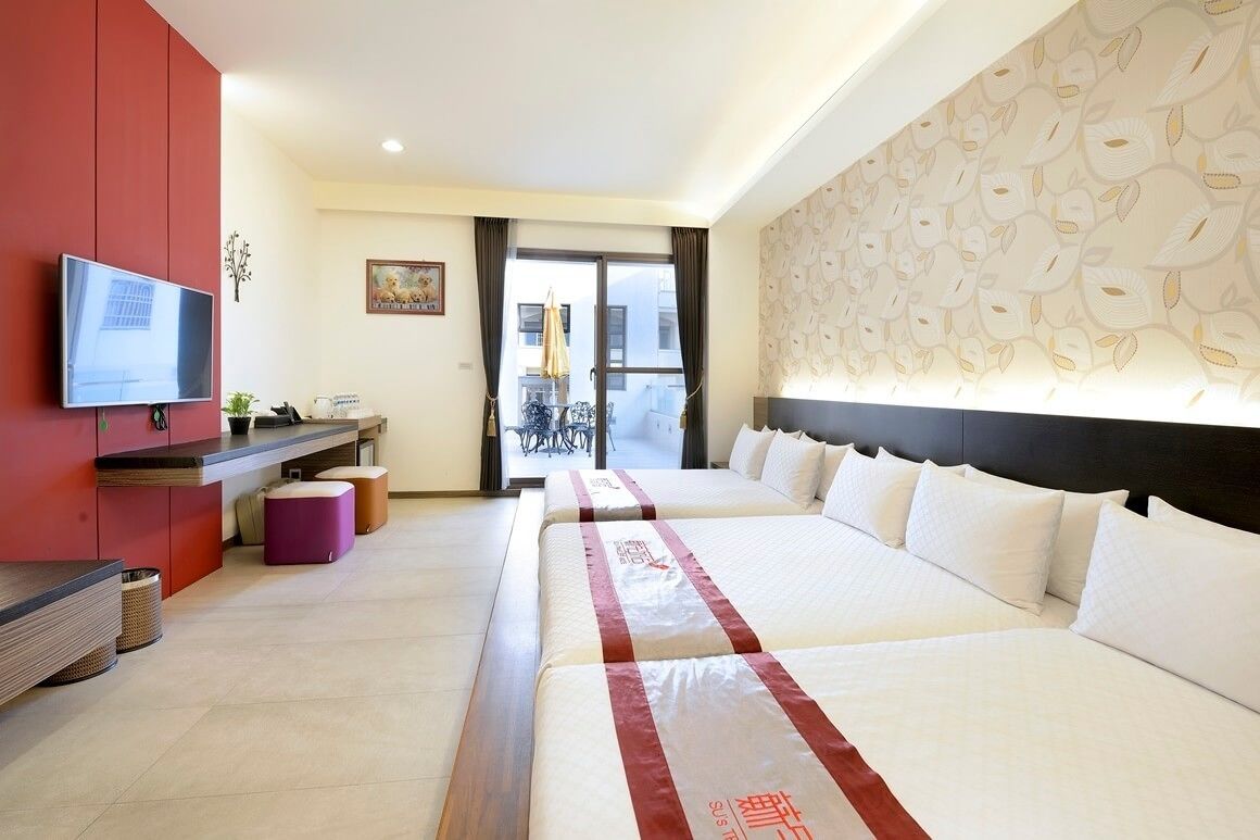 Quarto de hotel com duas camas, televisão, escrivaninha e vista para o exterior.