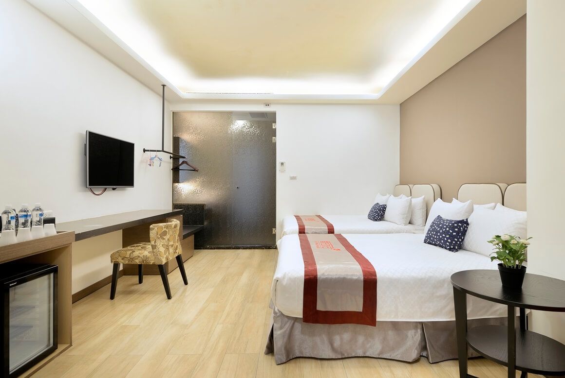 Habitación de hotel con cama, escritorio con silla, televisor y una pequeña mesa con planta.