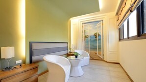 A hotel room with a bed, bedside table, lamp, and a view of the sea through a door.