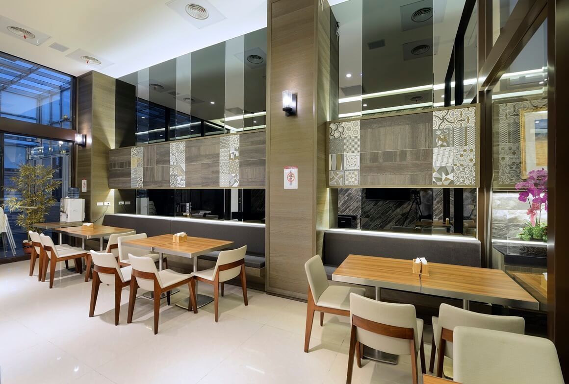 Un restaurante moderno con varias mesas y sillas, ventanas amplias y paneles decorativos en la pared.