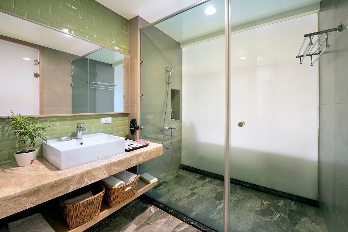 A modern bathroom with a glass-enclosed shower, a white sink, and a green tiled backsplash.