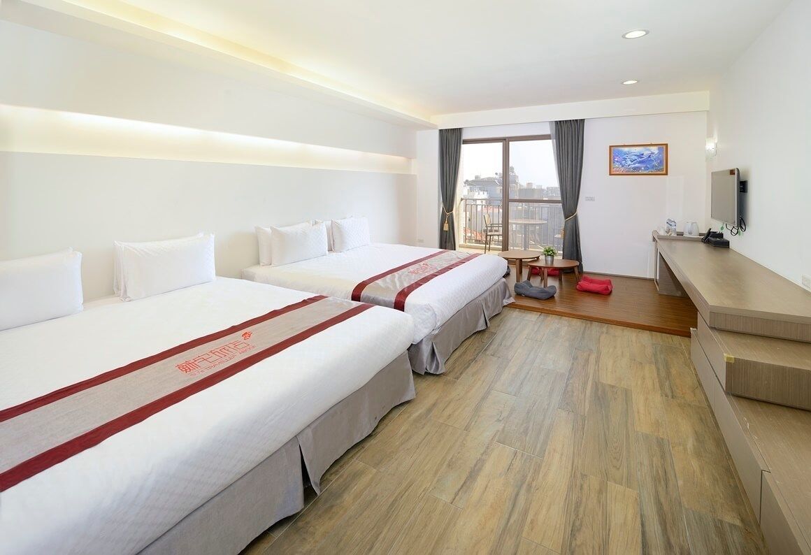 Ein Hotelzimmer mit zwei Betten, einem kleinen Tisch, einem Fernseher und einem Balkon mit Blick.