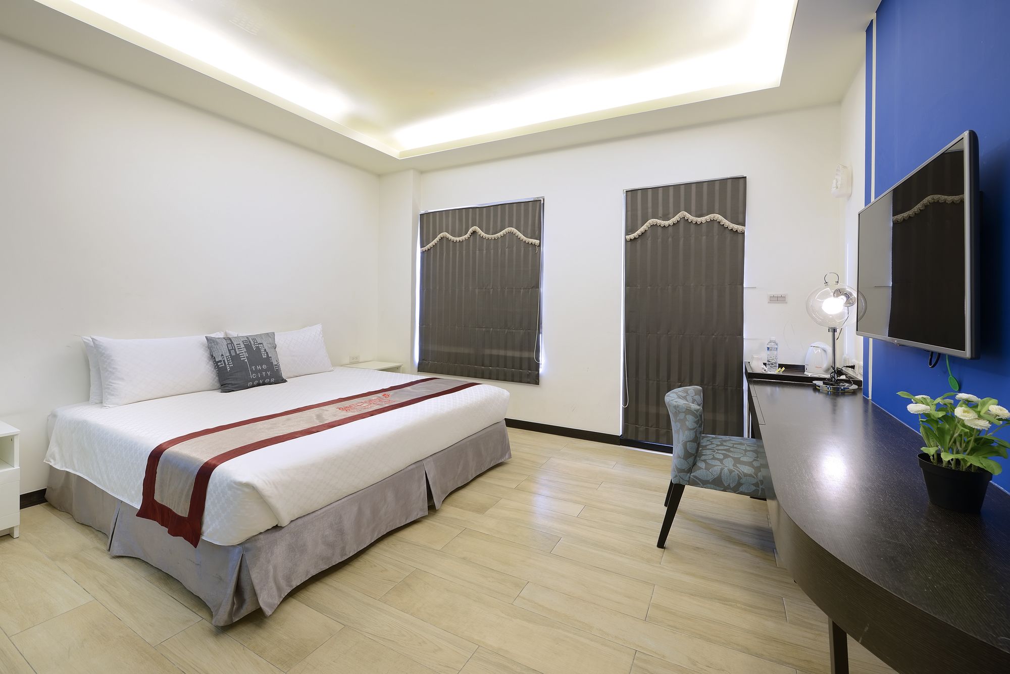Une chambre d’hôtel avec un lit, un bureau et une chaise, un miroir et une plante en pot.