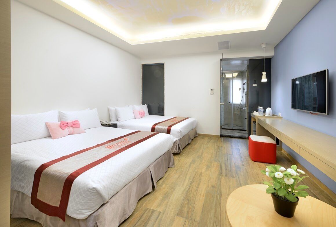 A hotel room with two beds, a small table with a plant, a TV, and a shower area.
