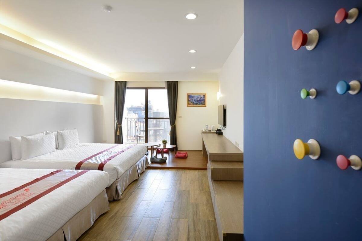 A hotel room with two beds, a desk, a chair, a TV, and a window with a view.