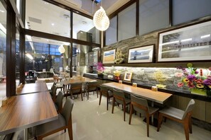 Uma área de jantar moderna com mesas e cadeiras de madeira, um painel de backsplash de pedra e quadros nas paredes.