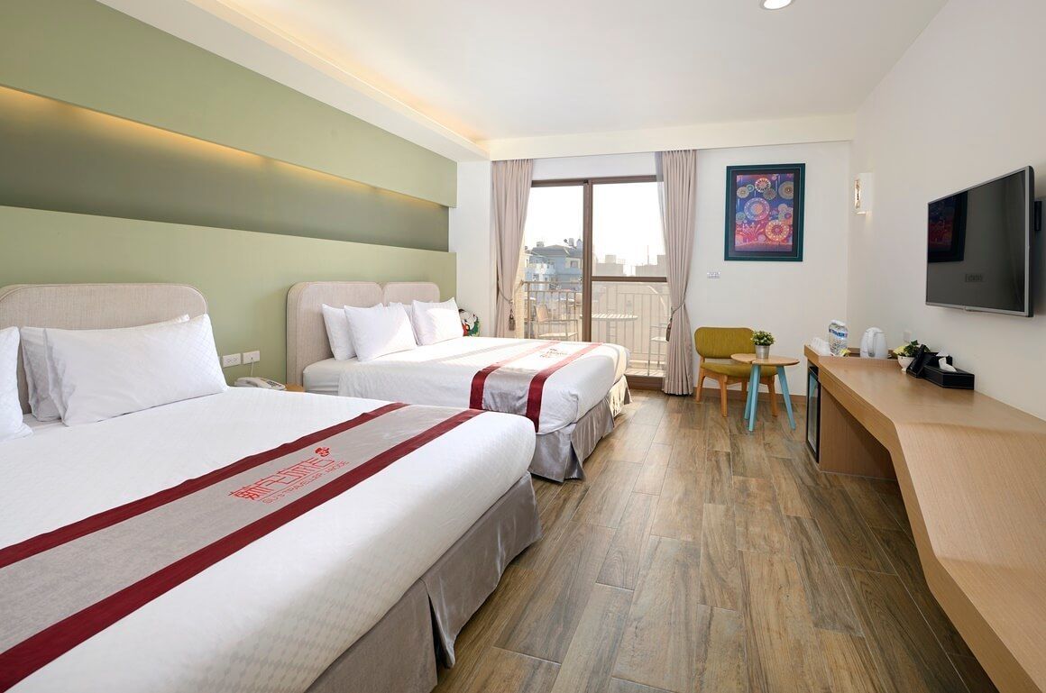 A hotel room with two beds, a desk, a chair, a TV, and a balcony with a view.