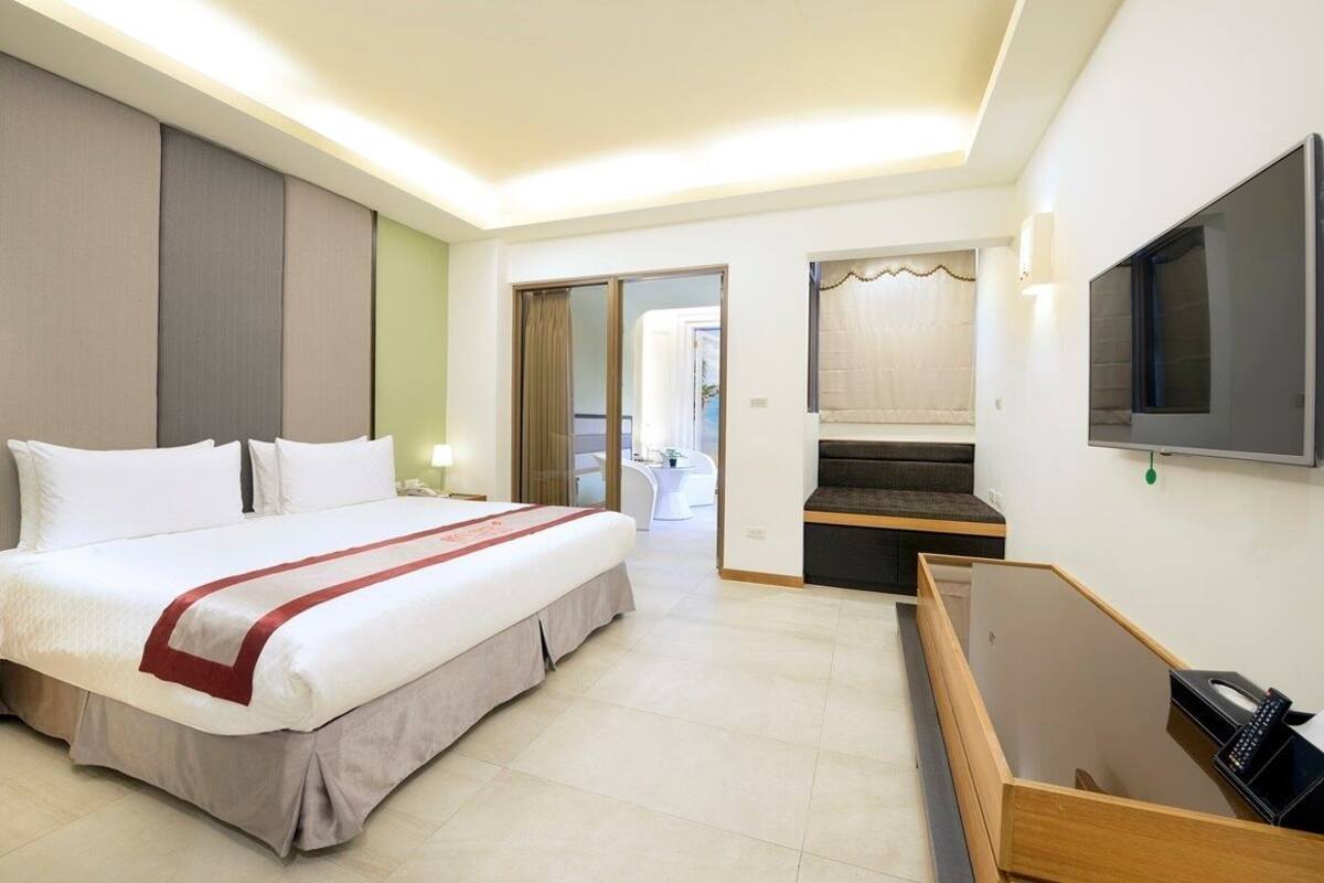 A hotel room with a large bed, a desk with a chair, a TV, and a view of the outside.