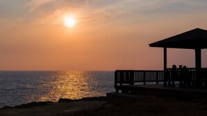 A beach scene with a gazebo overlooking the ocean during sunset.