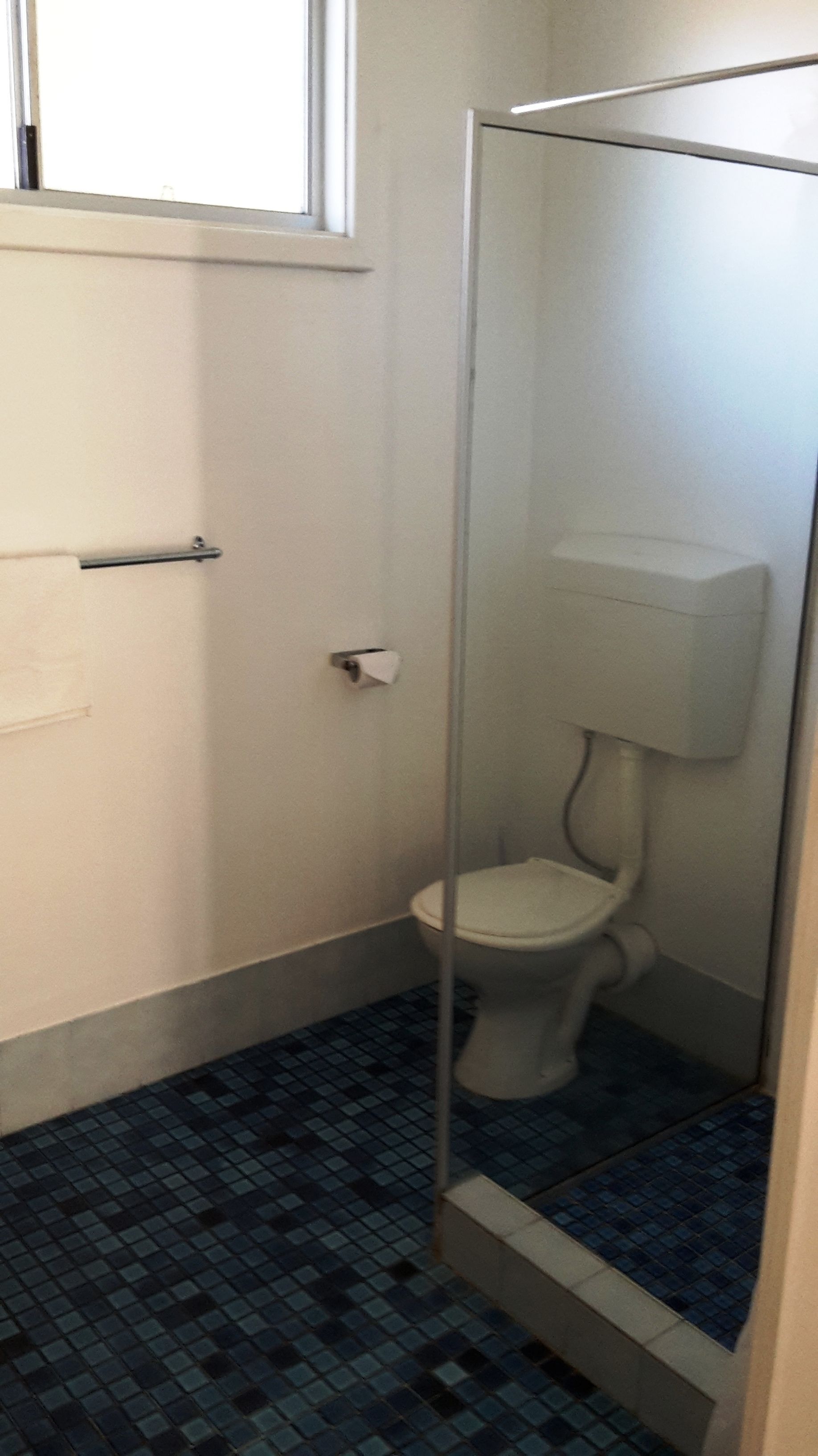Een kleine, smalle badkamer met toilet, handdroger en een raam boven het toilet.