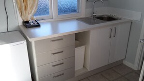 Cocina compacta con encimera blanca, pileta de acero inoxidable y lavavajillas integrado.