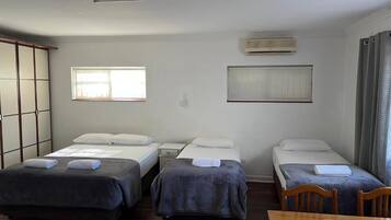 Una habitación de hotel con tres camas individuales, una mesa de madera y una puerta corredera.