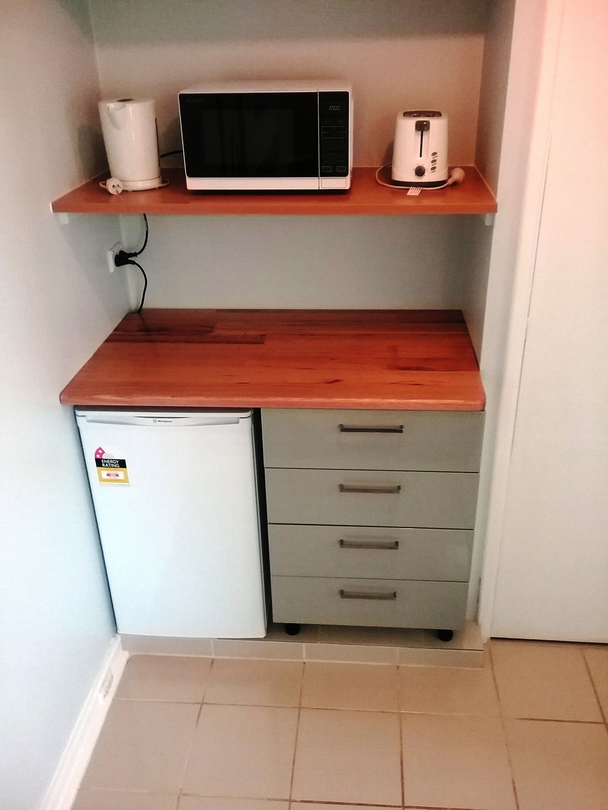 Cocina compacta con microondas, tostadora y refrigerador pequeño sobre una encimera de madera.