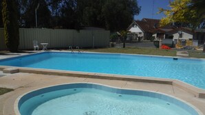 Una piscina rectangular con un jacuzzi en el centro, rodeada por una solana de hormigón.