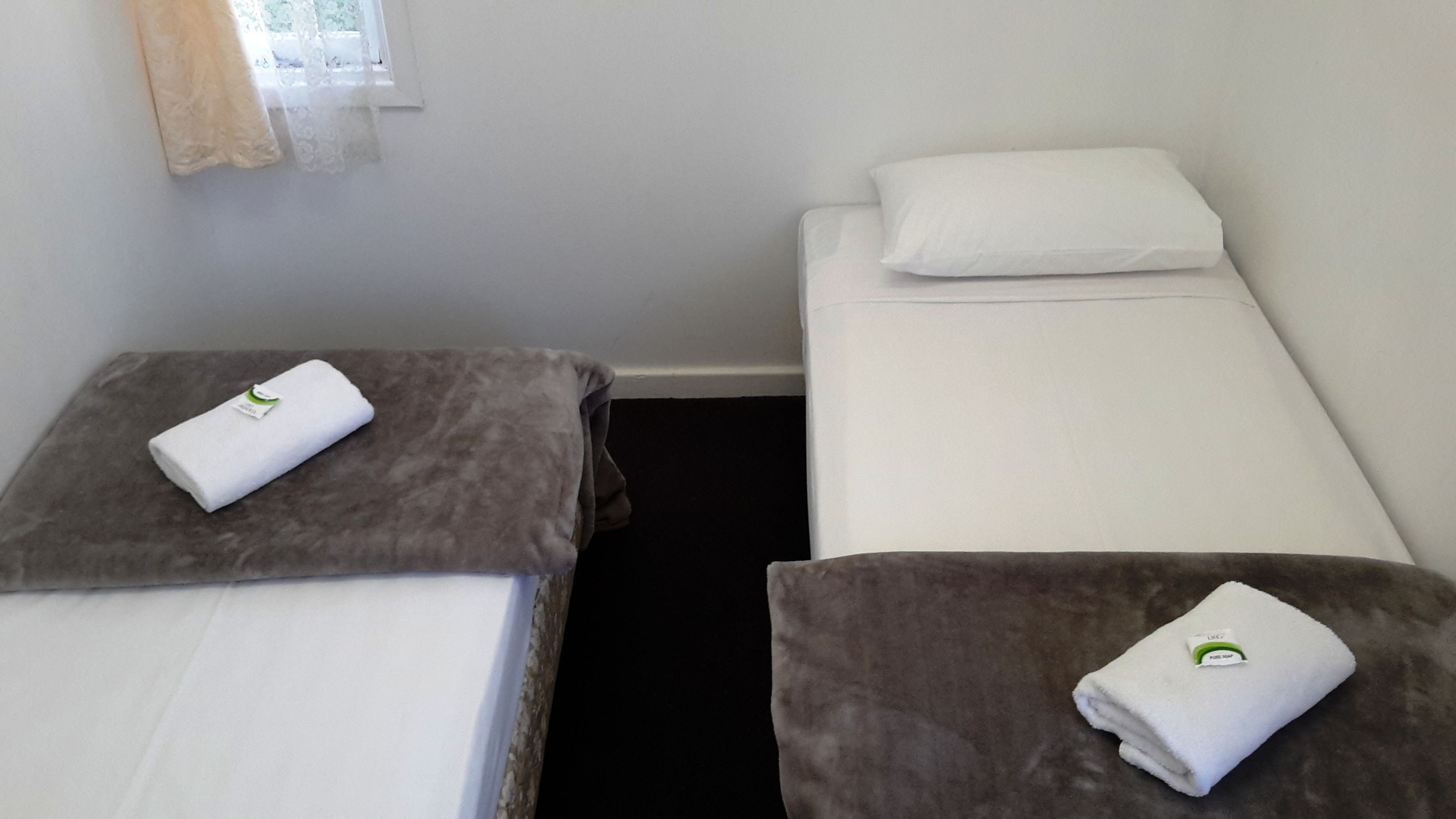 Una habitación pequeña y limpia con dos camas, cada una con una almohada y una toalla doblada.
