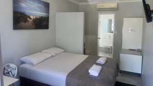 Habitación de hotel con cama, escritorio, silla, baño y televisor montado en la pared.