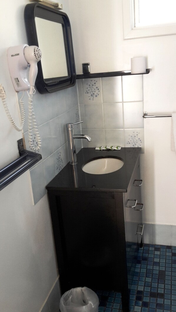 Un baño con un lavabo negro, un secador de pelo y un espejo.