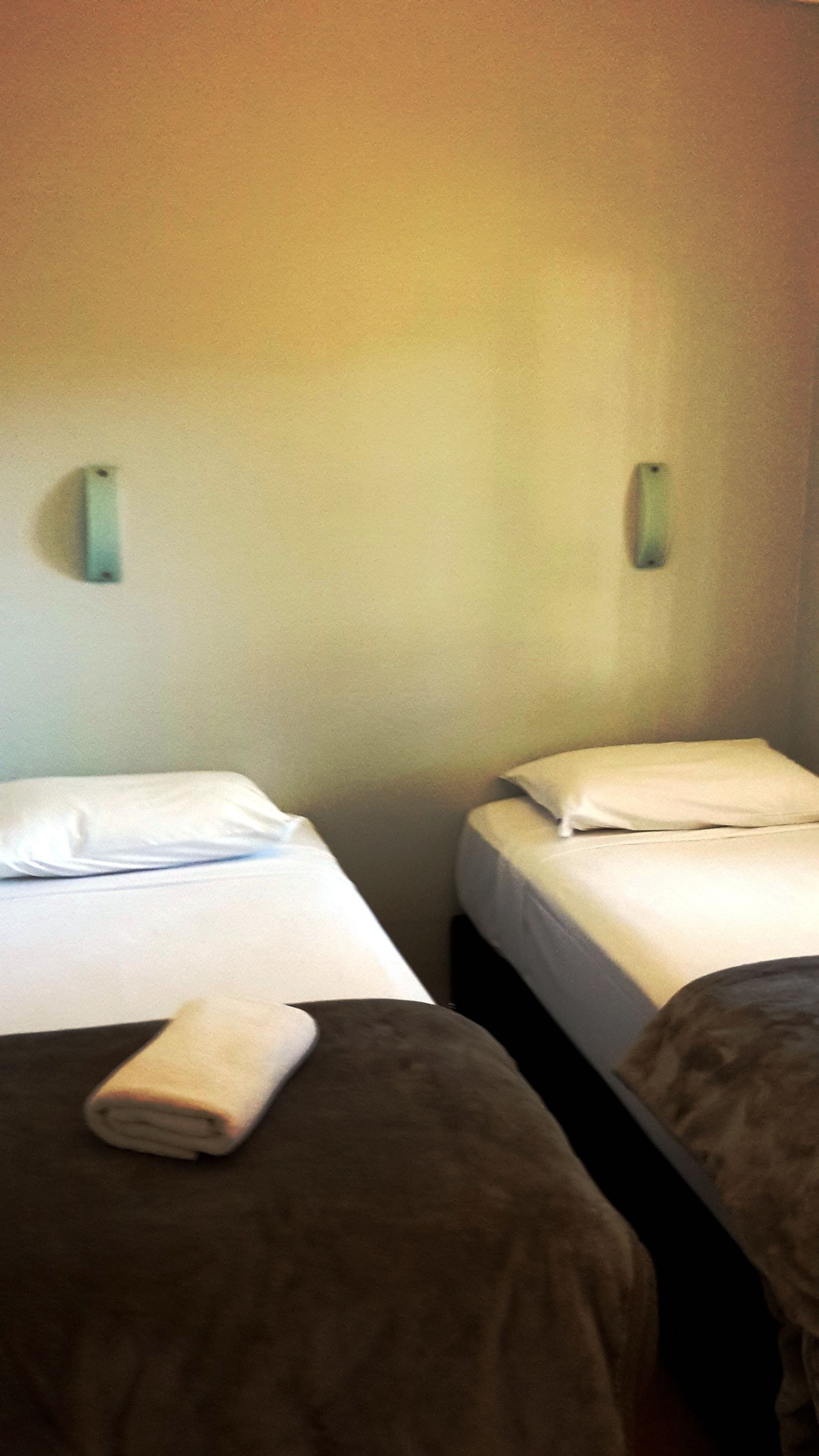 A hotel room with two beds, each with white linens and pillows, and a brown blanket on the left bed.