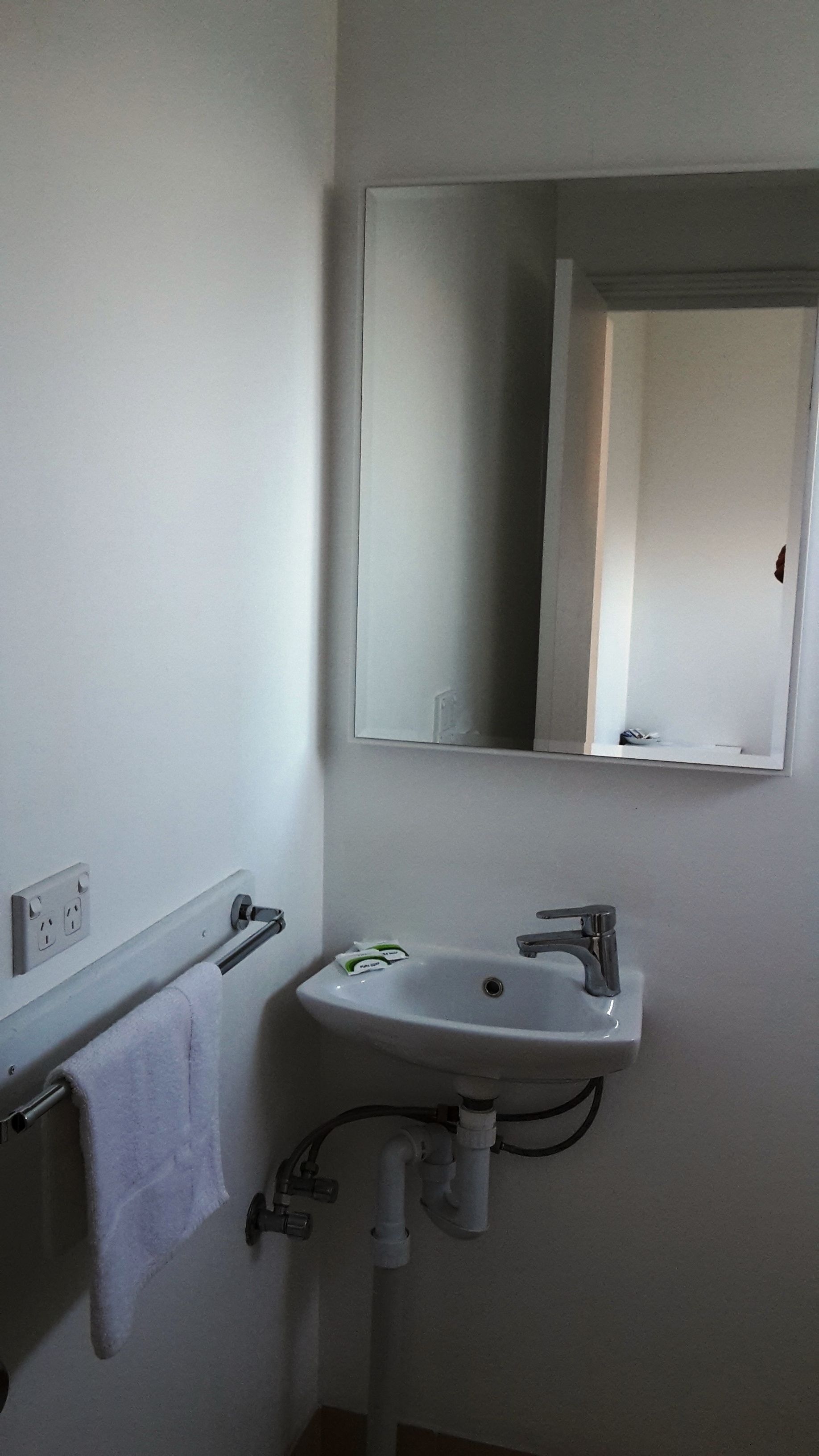 Un baño con un lavamanos blanco, un espejo y un perchero para toallas.