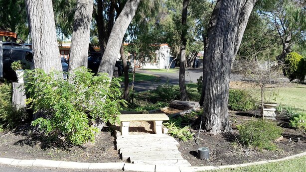 Un banco de piedra en un área ajardinada con árboles y un camino pavimentado.
