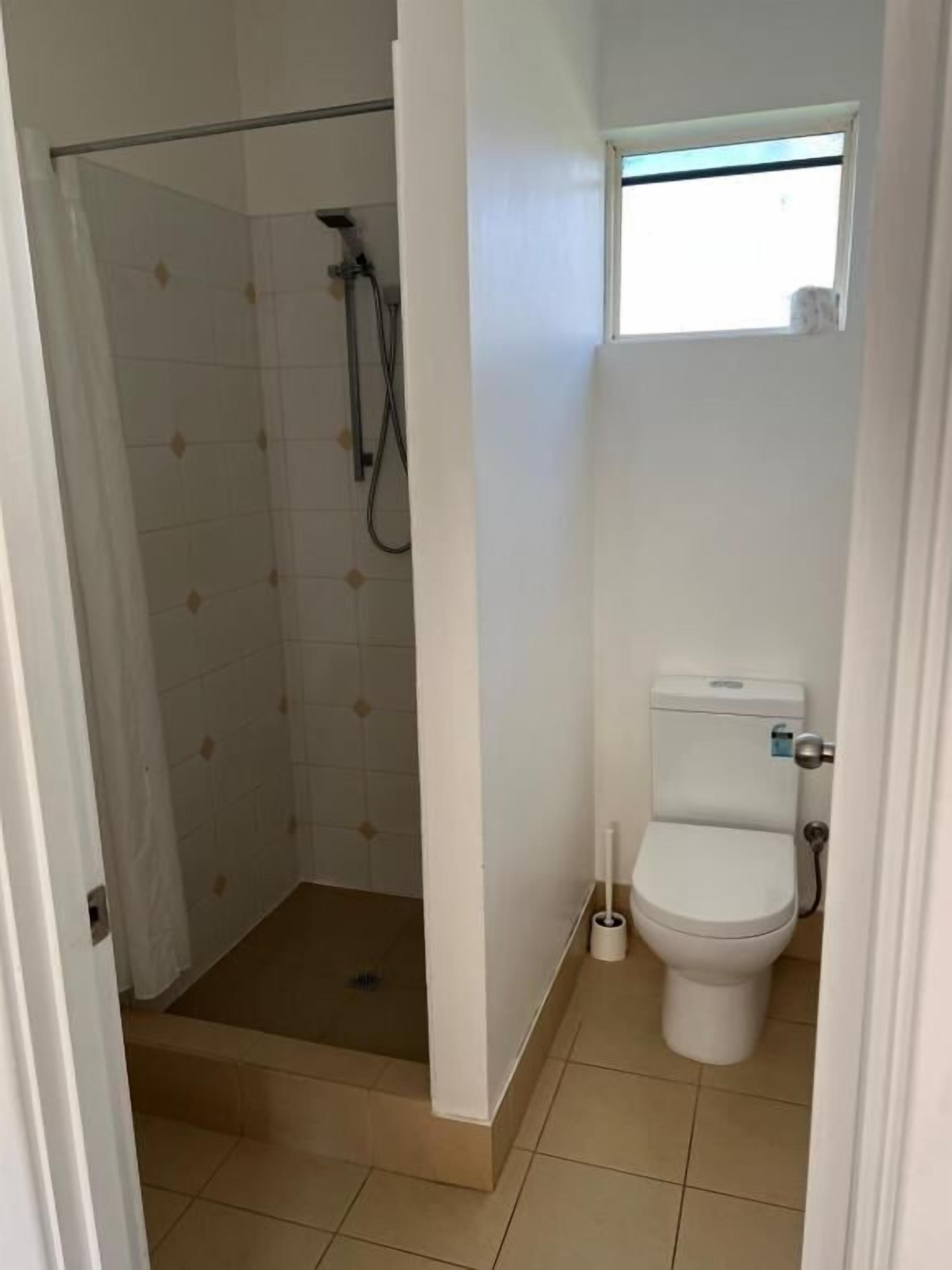 Un baño pequeño con ducha, inodoro y ventana sobre el inodoro.