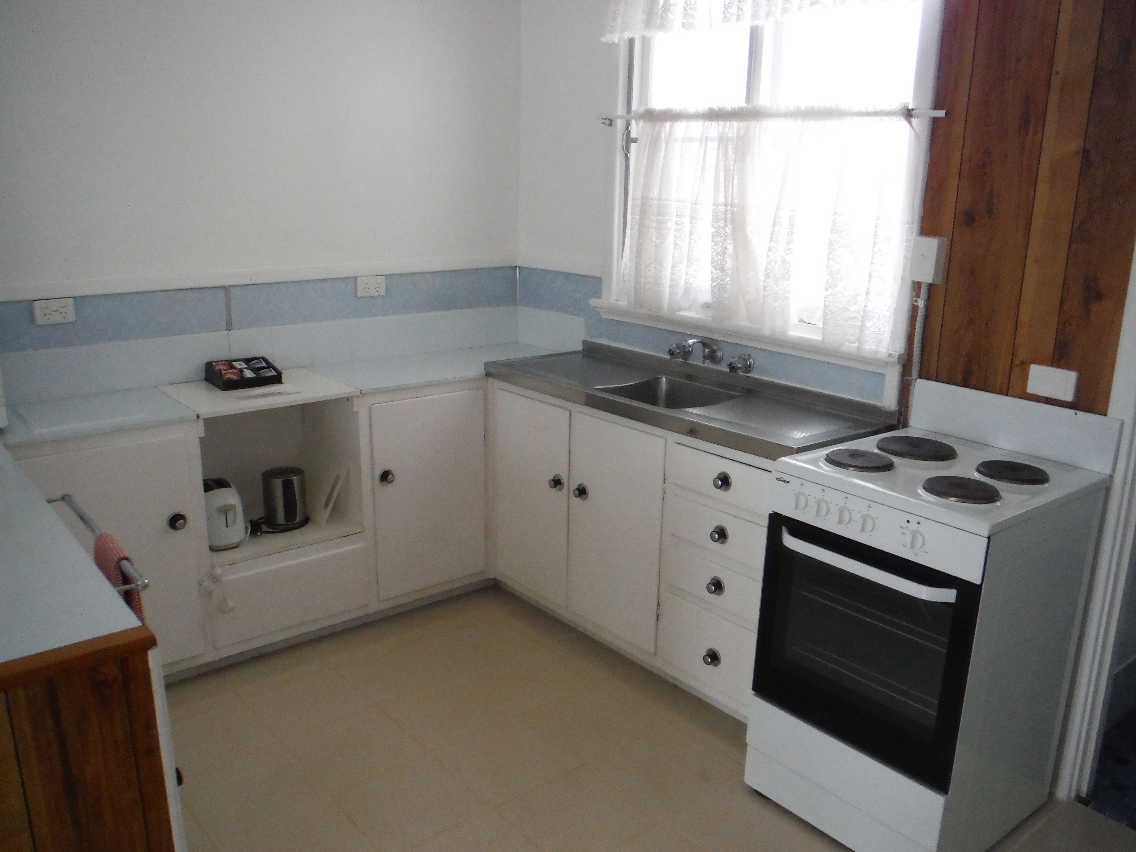A compact kitchen with a white stove, a sink, and a window with curtains.