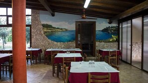 Un restaurante con mesas dispuestas para comer, un mural con una escena costera en la pared y un ventilador de techo.