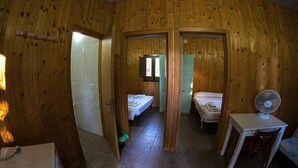Habitación pequeña con paredes de madera, una cama, una mesita con un ventilador y una ventana.